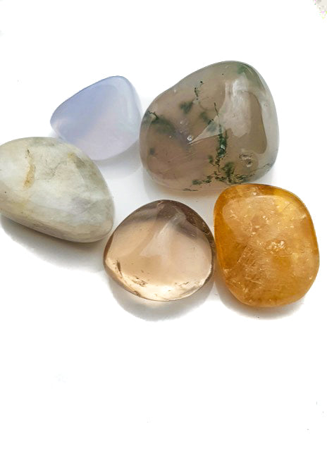 A collection of five tumble stones on a white background. These stones are green moss agate, smoky quartz, moonstone, blue chalcedony and honey calcite