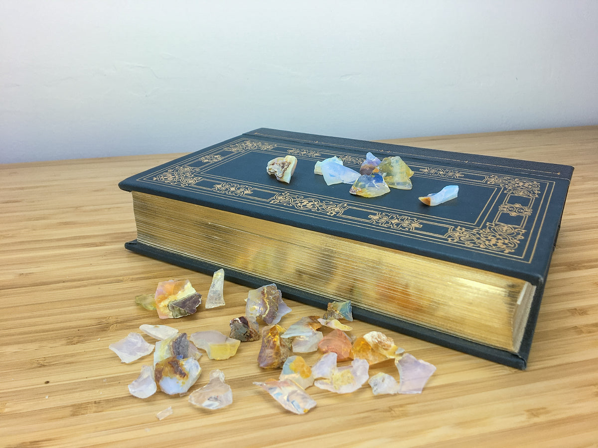 blue opalescent chips of raw Ethiopian fire opal on a black leatherbound book. A further cluster of raw opals are on a light wood grained surface