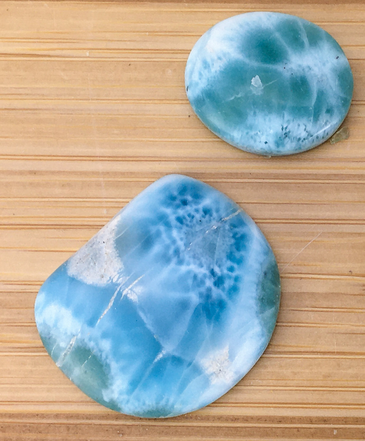 two Larimar cabochons on a wood grain surface. The Larimar is a watery blue