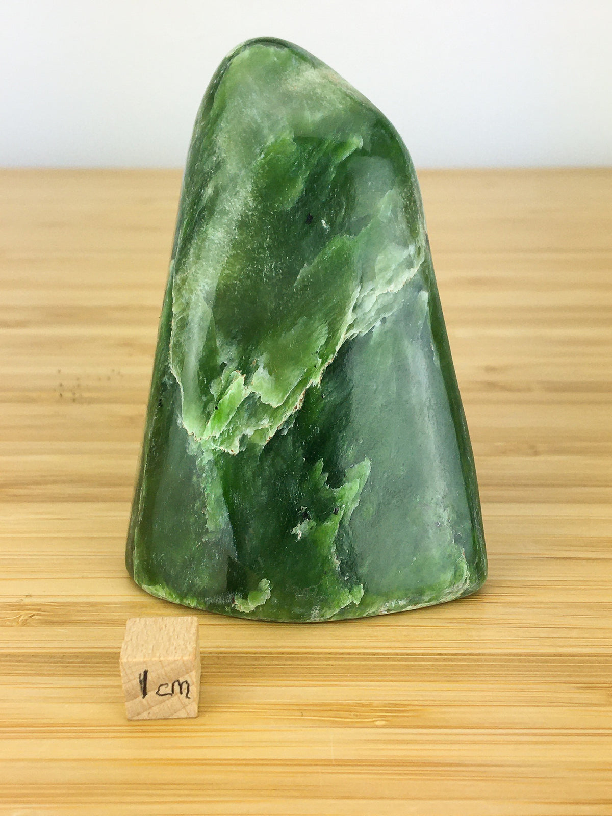 nephrite jade freeform. It is a vivid green and has streaks of white actinolite and talc. It is shown next to a 1cm cube for scale, It is about 6cm wide and 8cm high