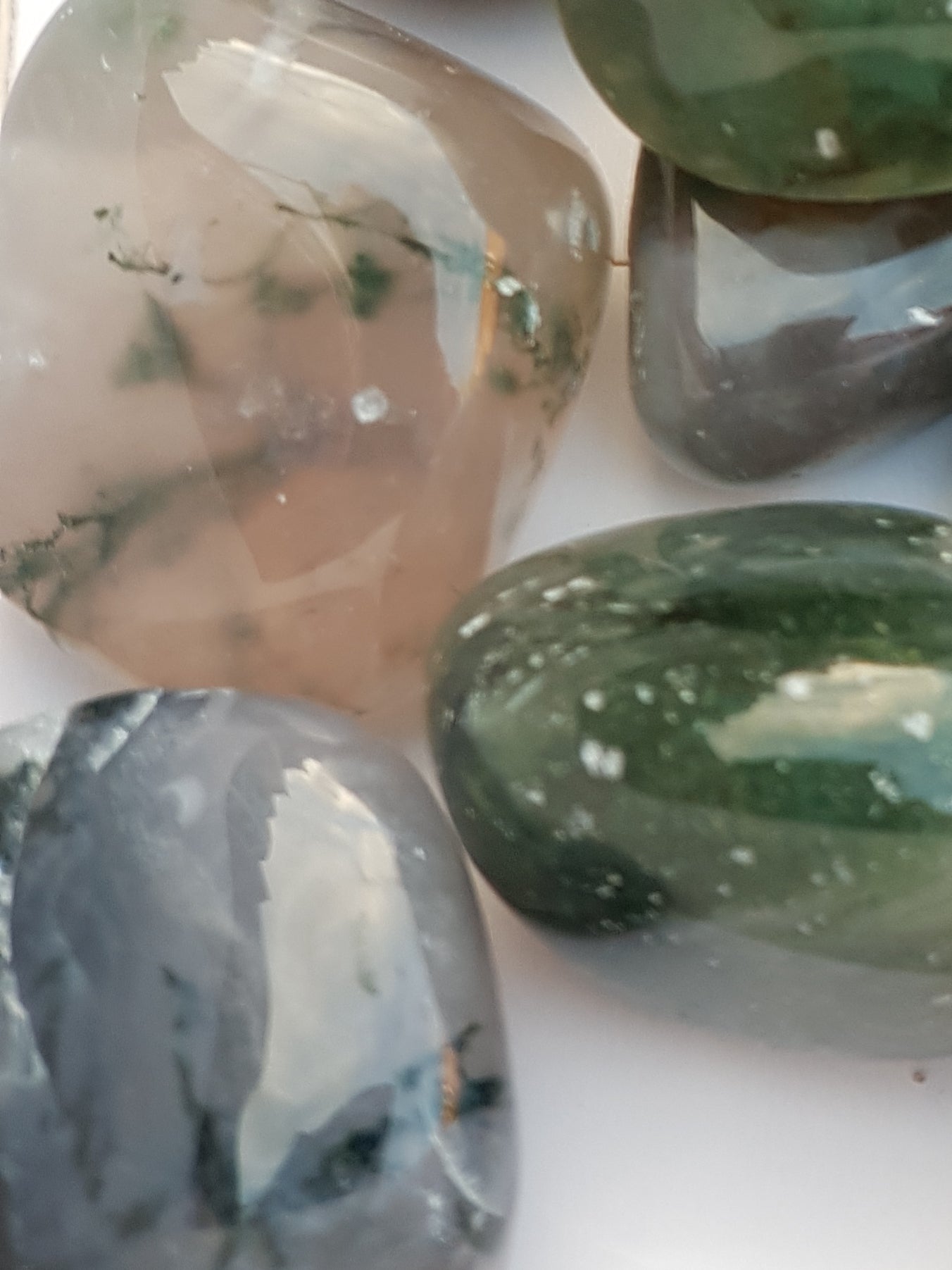 a close up of three tumbled pieces of green moss agate. The pieces are translucent and clear. Inside the stone are strands of a dark green material.