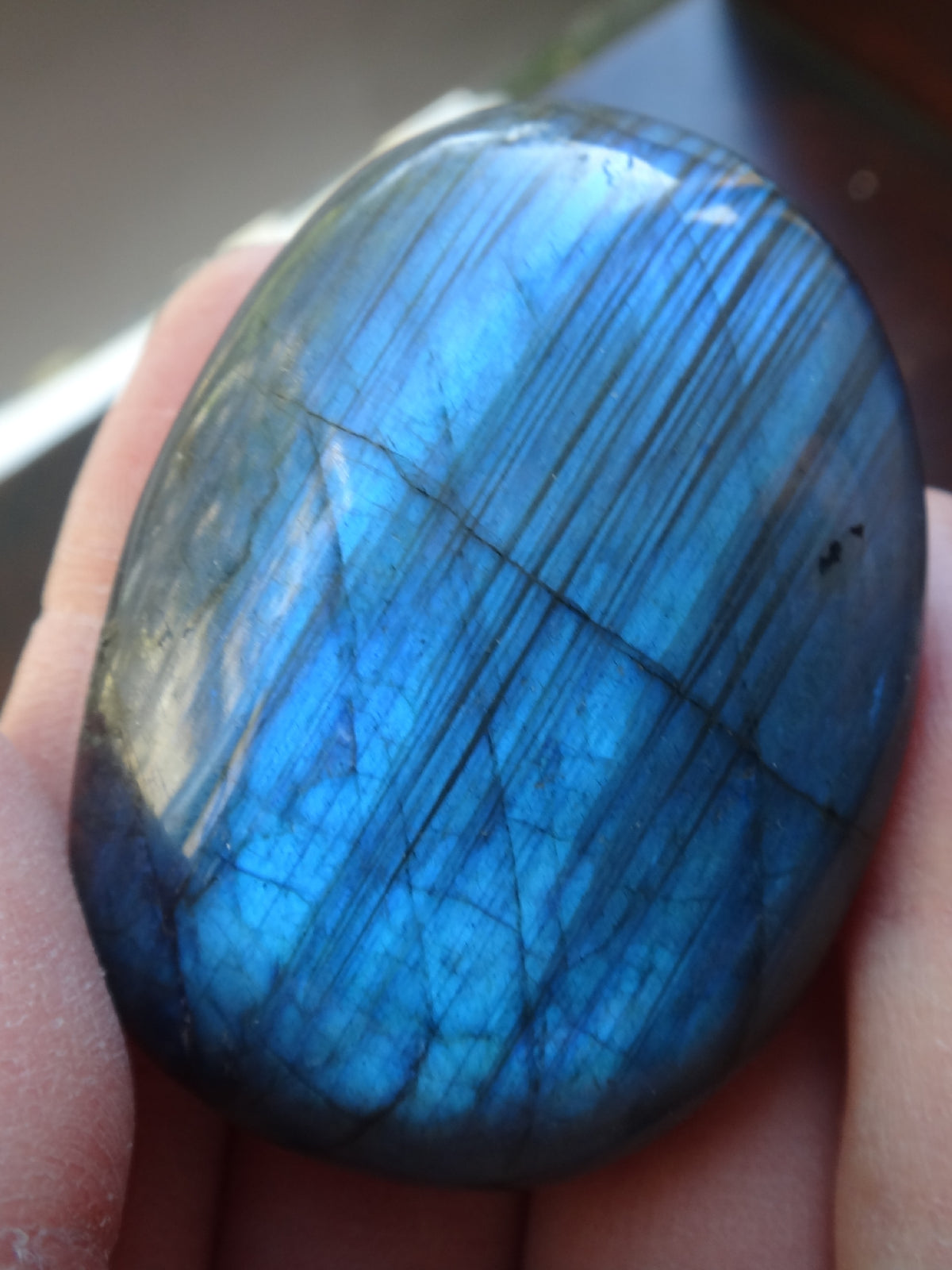 a labradorite palmstone held in a hand. The piece has blue labradorescence. It is showing distinct lamella twinning
