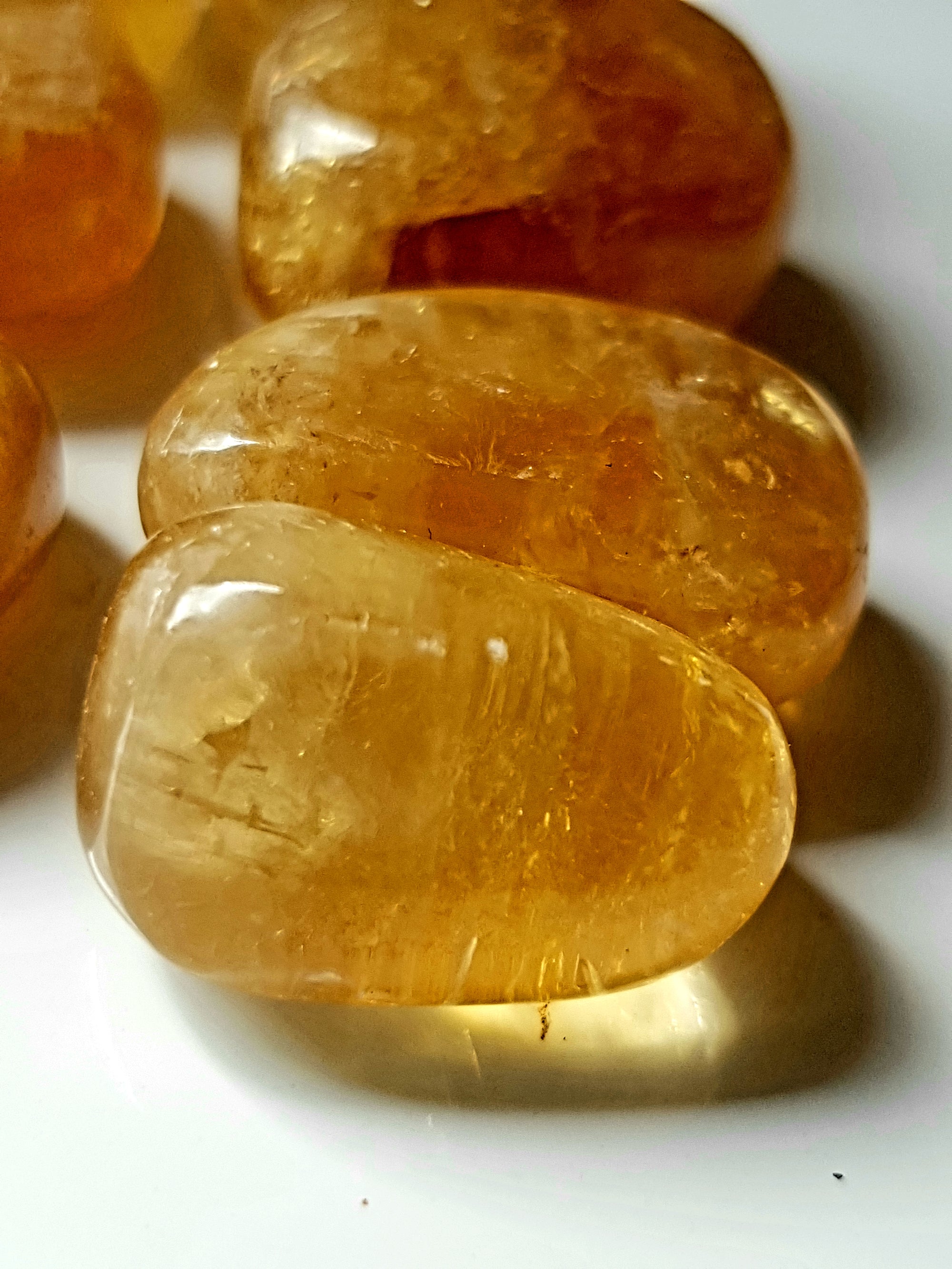 three tumbled pieces of honey coloured calcite. The pieces are very translucent and light is projected through them to give a golden glow on the surface beneath.