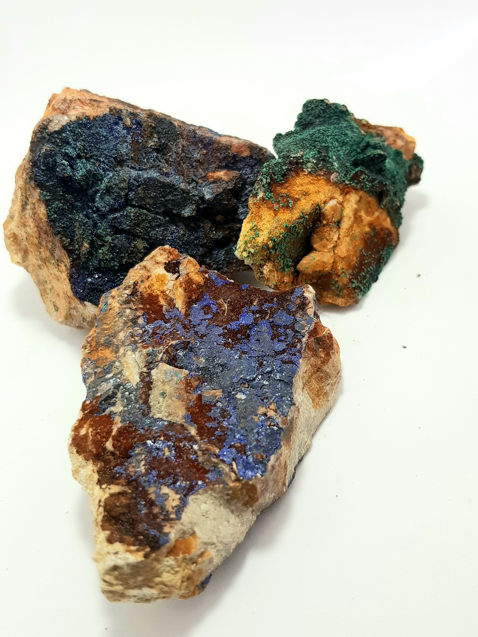 three pieces of raw azurite and malachite on the matrix. vibrant blue and green crystals on a beige carbonate matrix