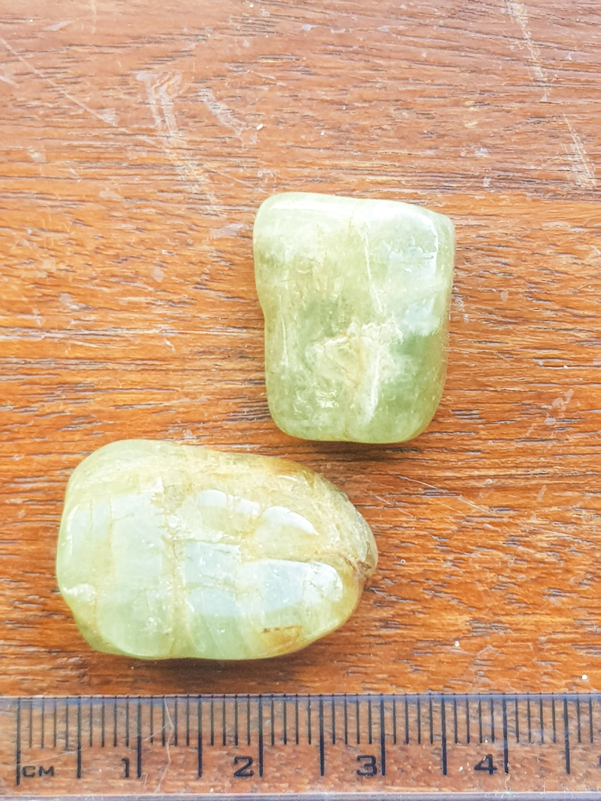 two green aquamarine tumblestones. They are placed against a ruler for scale. They are about 2.5cm long.