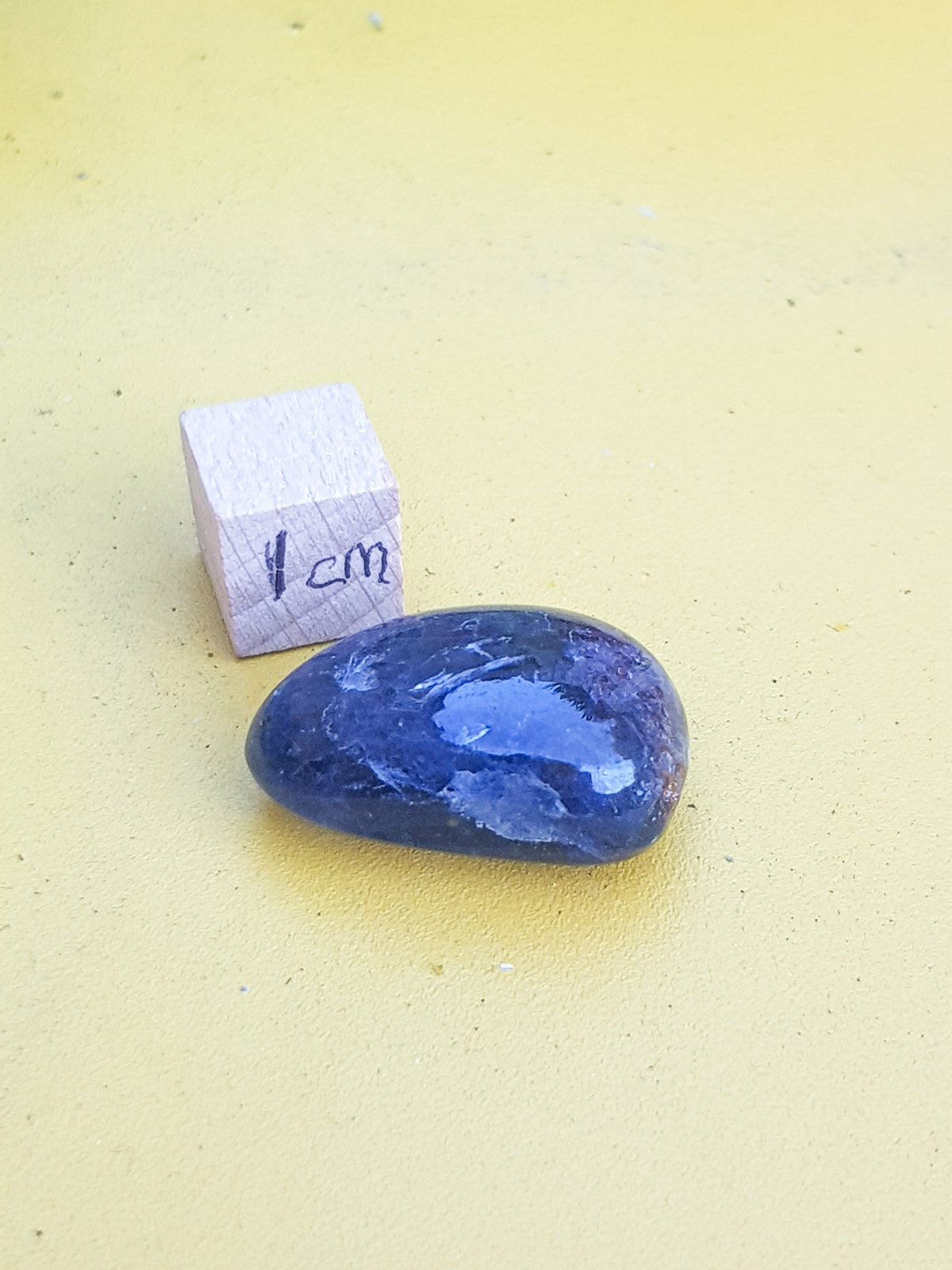 Small polished sample of Iolitye next to a 1cm cube for scale. It is approximately 2cm along its longest axis. The sample appears to be dark blue, but this is primarily an artifact of photography and is due to contrast correction. on the camera. The true shade is a little lighter.