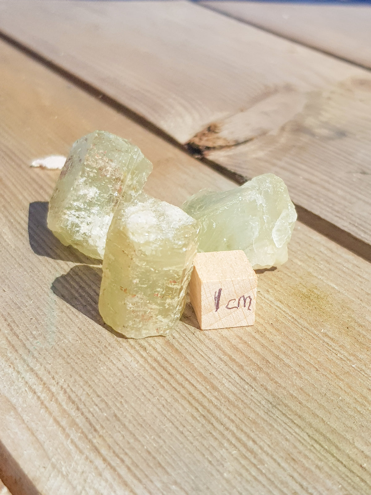 three beryl crystals. They are hexagonal. they are yellow/green. They are next to a ruler for scale. They are about 1.2 cm tall and 1cm wide.