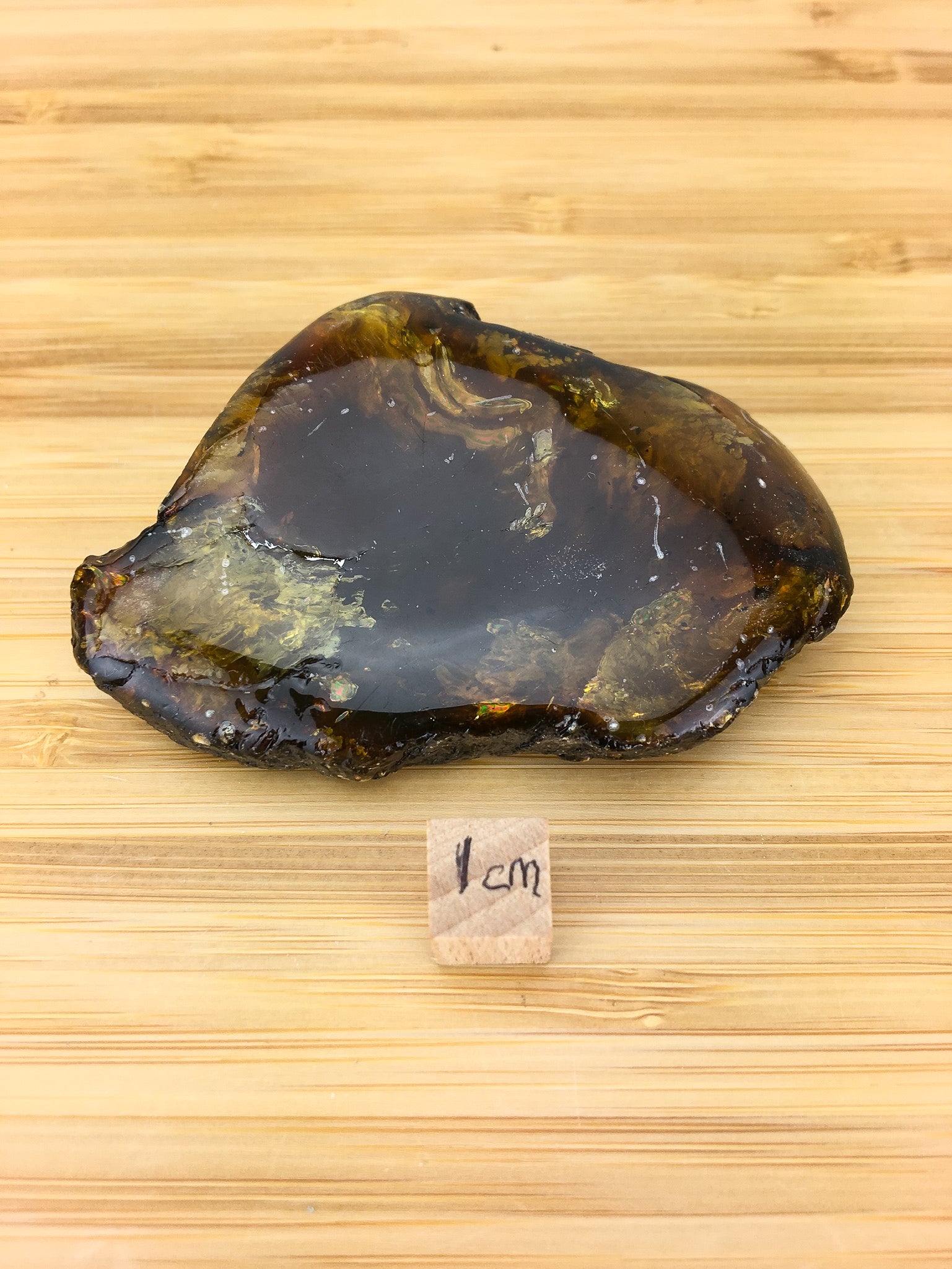 a polished chunk of Amber from Sumatra. The sample is next to a 1cm cube for scale. It is about 6cm long and 4 cm wide