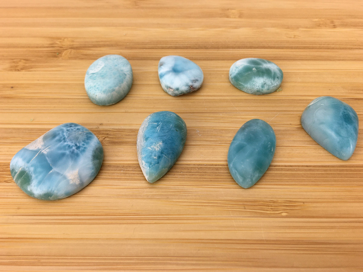 several Larimar cabochons on a light wood grained surface. The malrimar is watery blue.