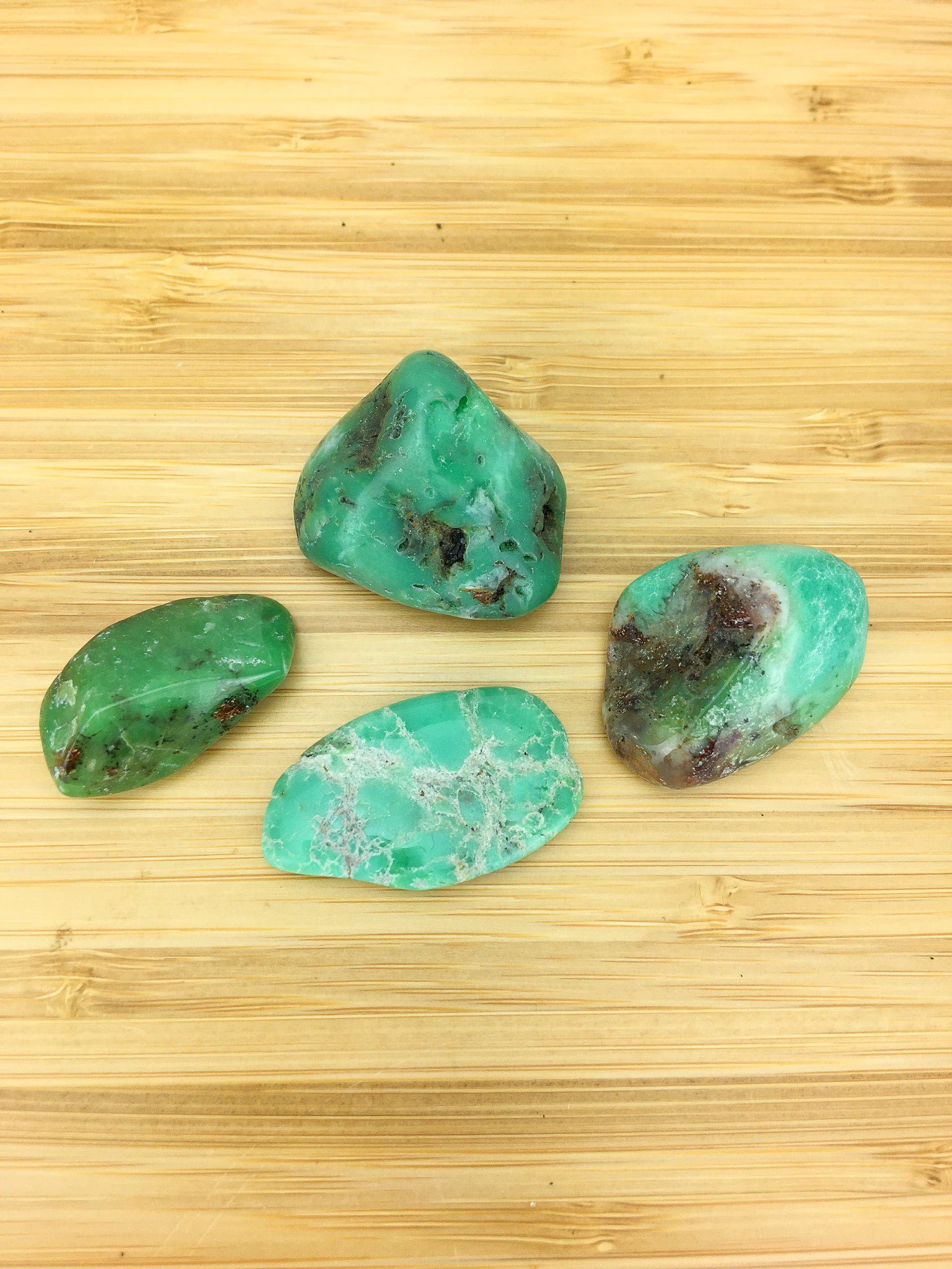four pieces of apples green chrysoprase on a light wood grained surface