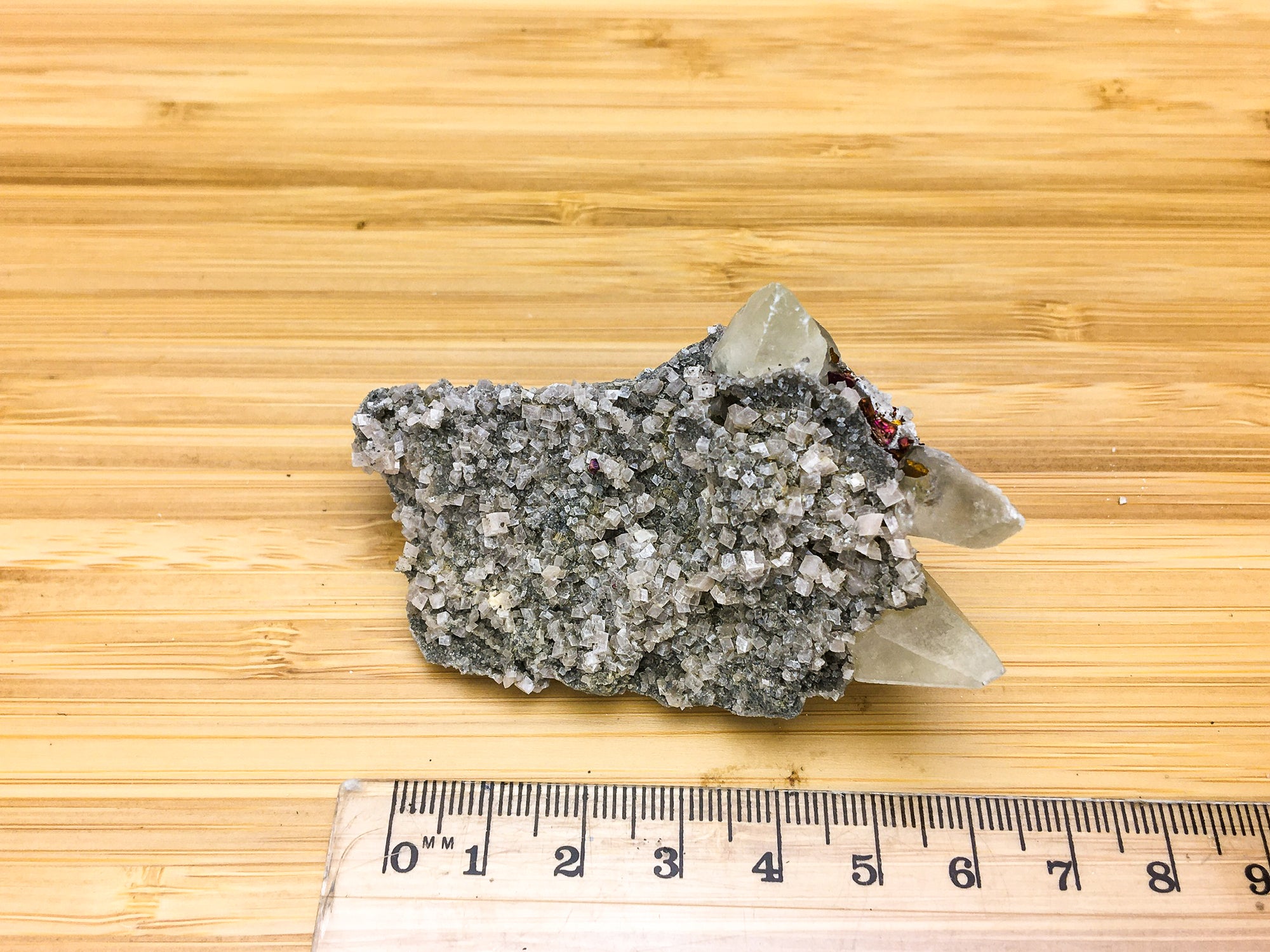 A sample of druzy rhombic calcite crystals placed next to a ruler . The sample is 6cm long.