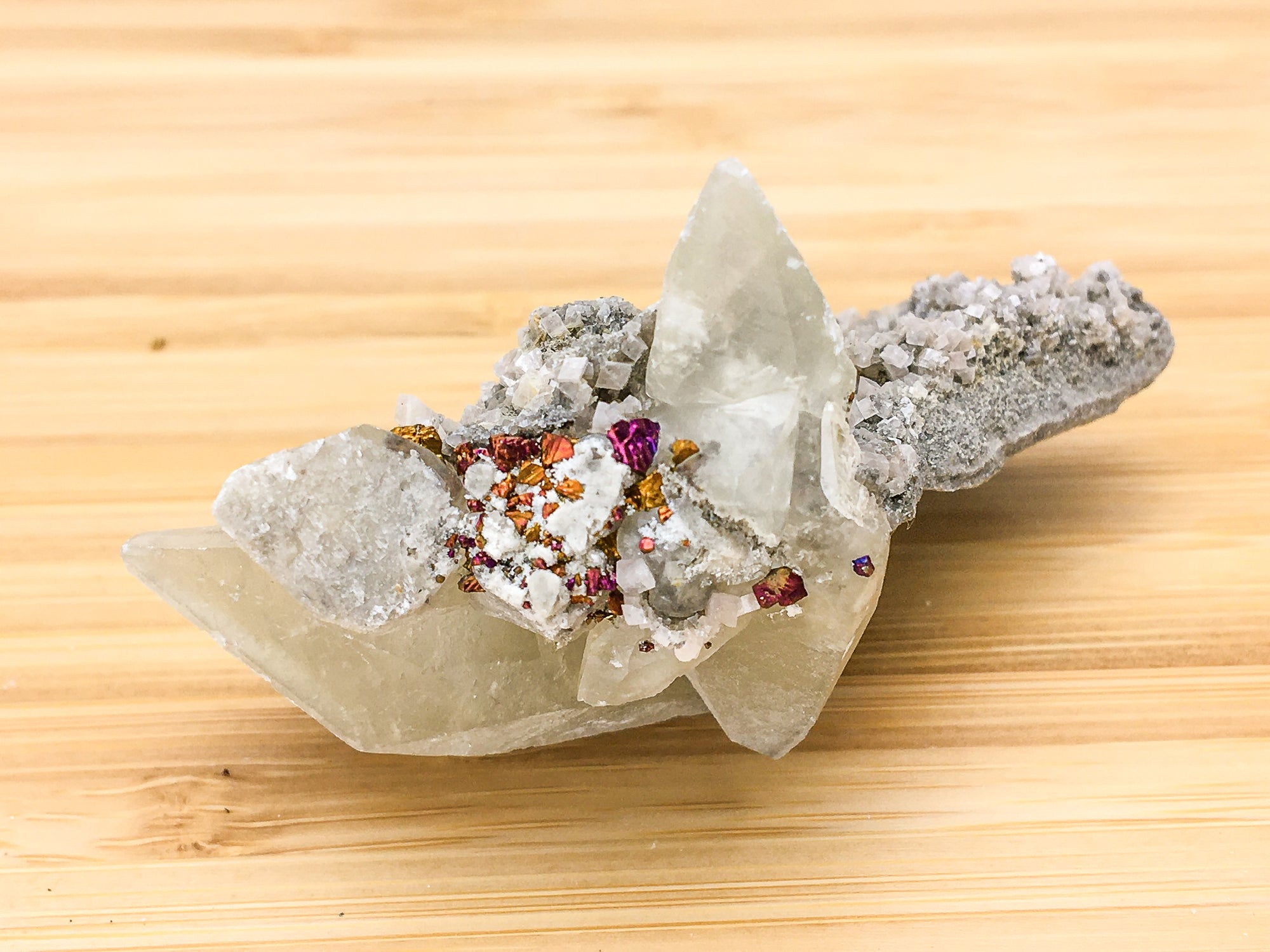 twinned double terminated dogtooth calcite crystals. They have an overgrowth of rhombic calcite crystals on the right hand long axis of the sample. There is a population of purple and orange oxidised chalcopyrite crystals in the centre of the sample.