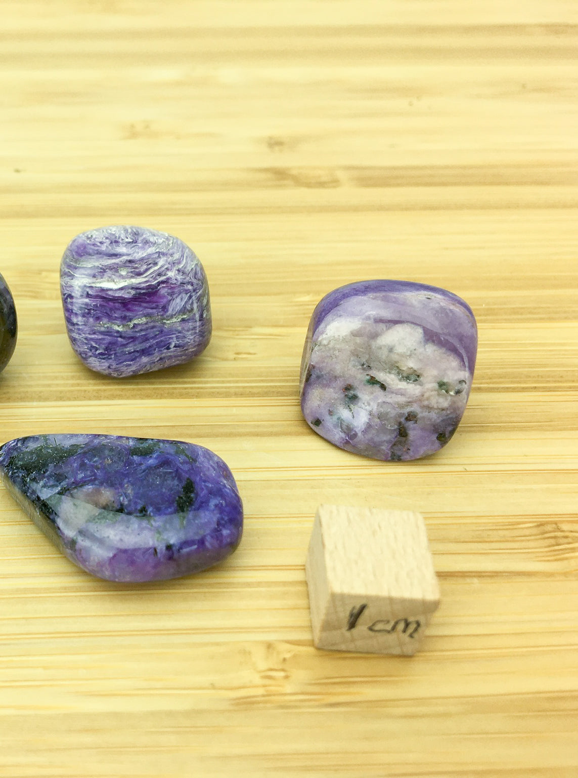 three chariot tumble stones. They are a rich purple with some white banding. A 1cm cube is in the ophotgraoh for scale. The samples are about 1cm each.