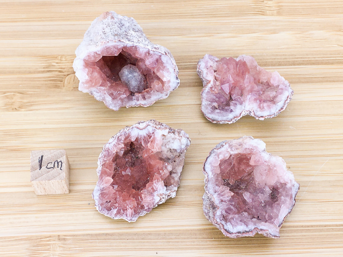 four pink amyethyst crystals, they are placed next to a 1cm cube for scale. The pieces are about 4x4cms in size
