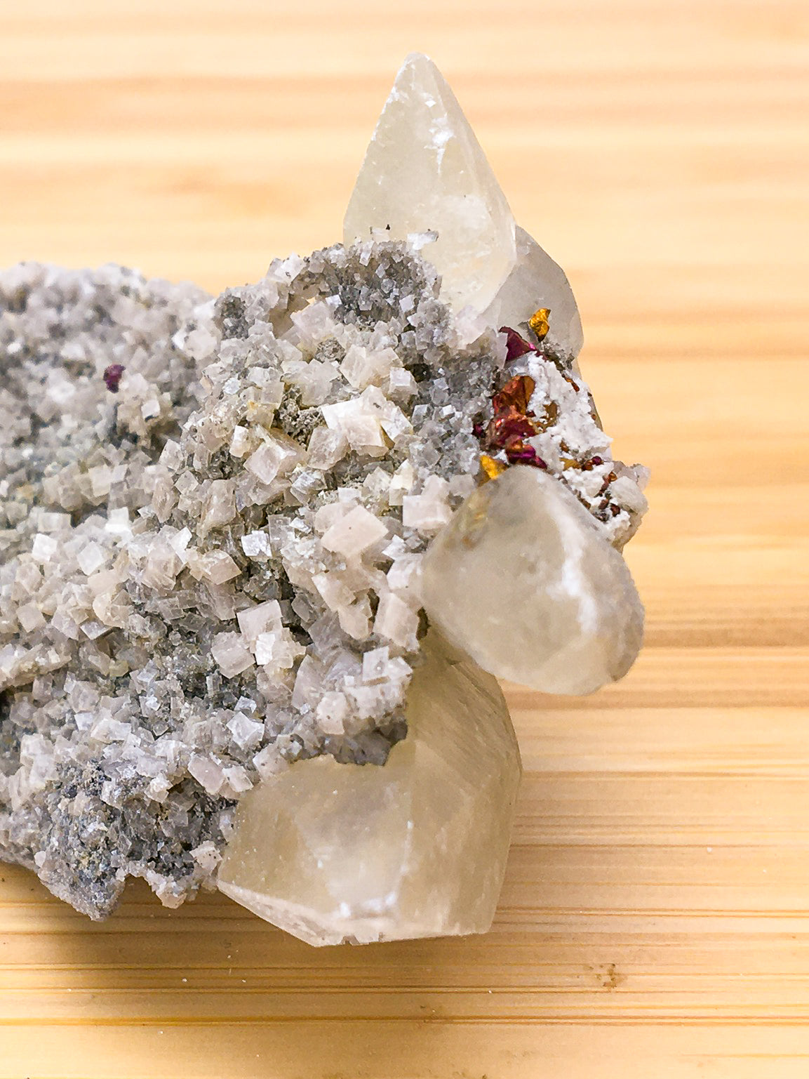 translucent white dogtooth calcite, with an overgrowth of rhombic calcite crystals. a small population of  oxidised chalcopyrite crystals are present on the surface of the upper right hand section of the sample. They are red and orange and iridescent.
