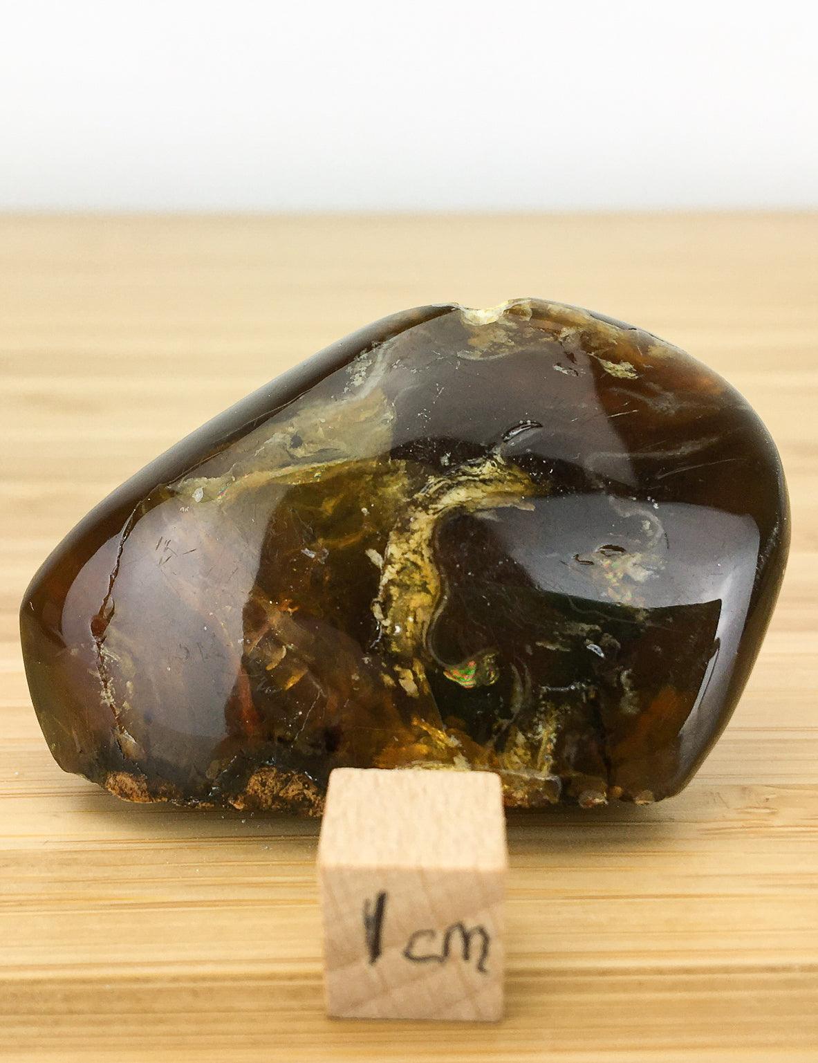 polished Amber from Sumatra. It is very translucent and an orangey brown. It is placed next to a 1cm cube. The sample is about 5cm