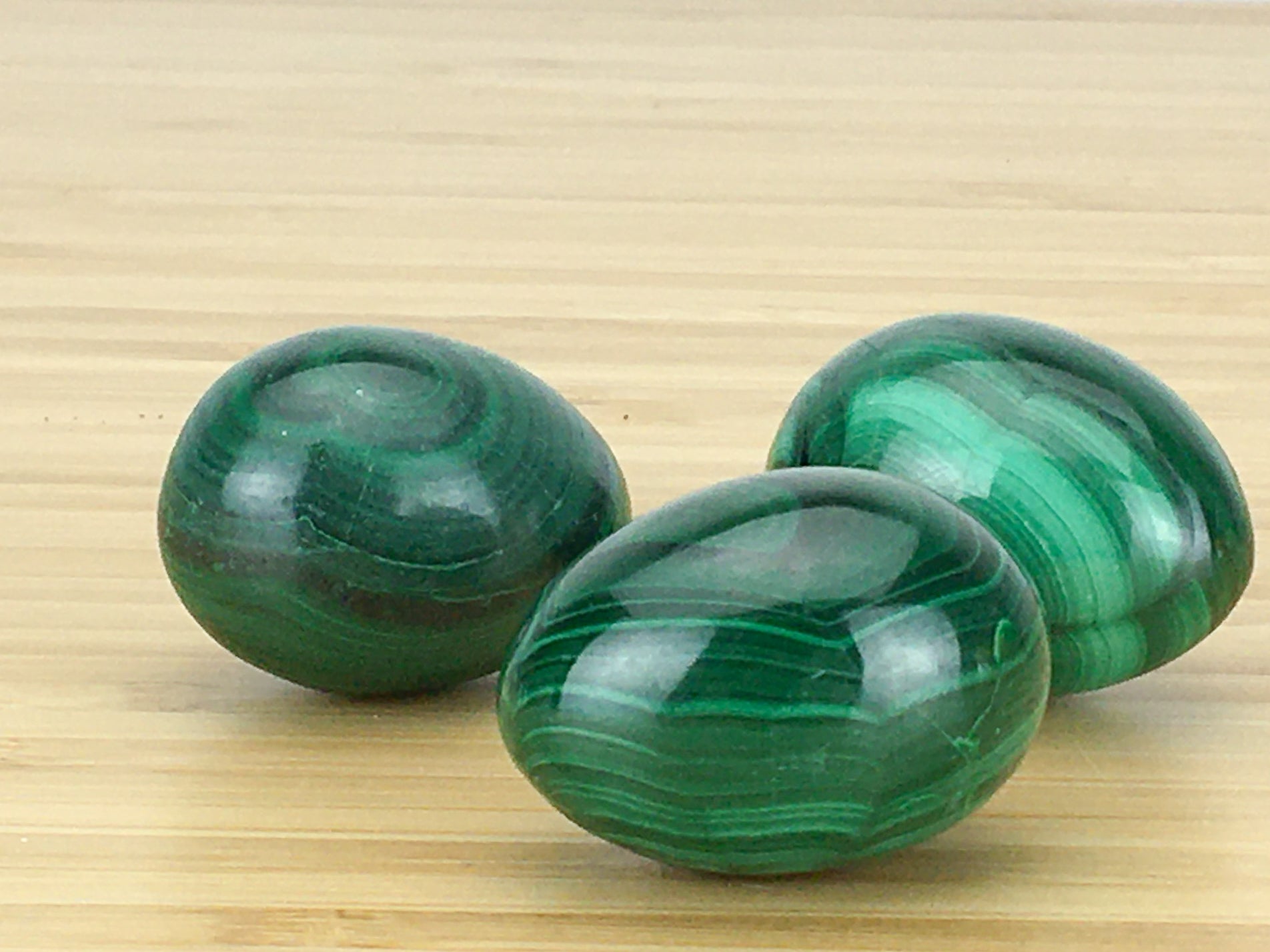 three malachite eggs on a light wood grain surface