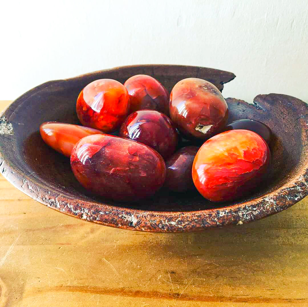 A number of carnelian pebbles in a hand carve wooden bowl.