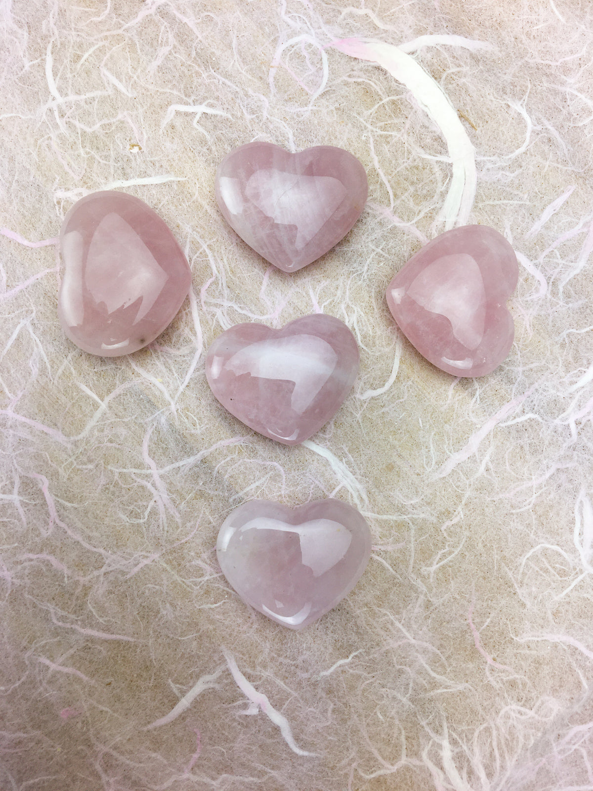 five rose quartz hearts on a  white gauze background