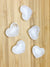 five selenite hearts on a light grained wood surface.
