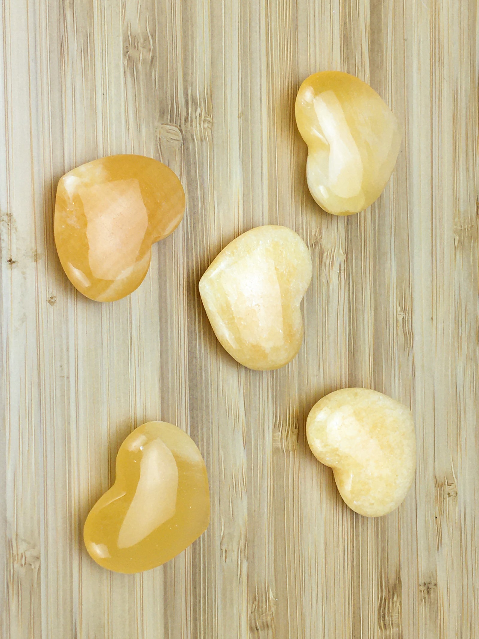 five orange calcite hearts on a light wood  grained surface