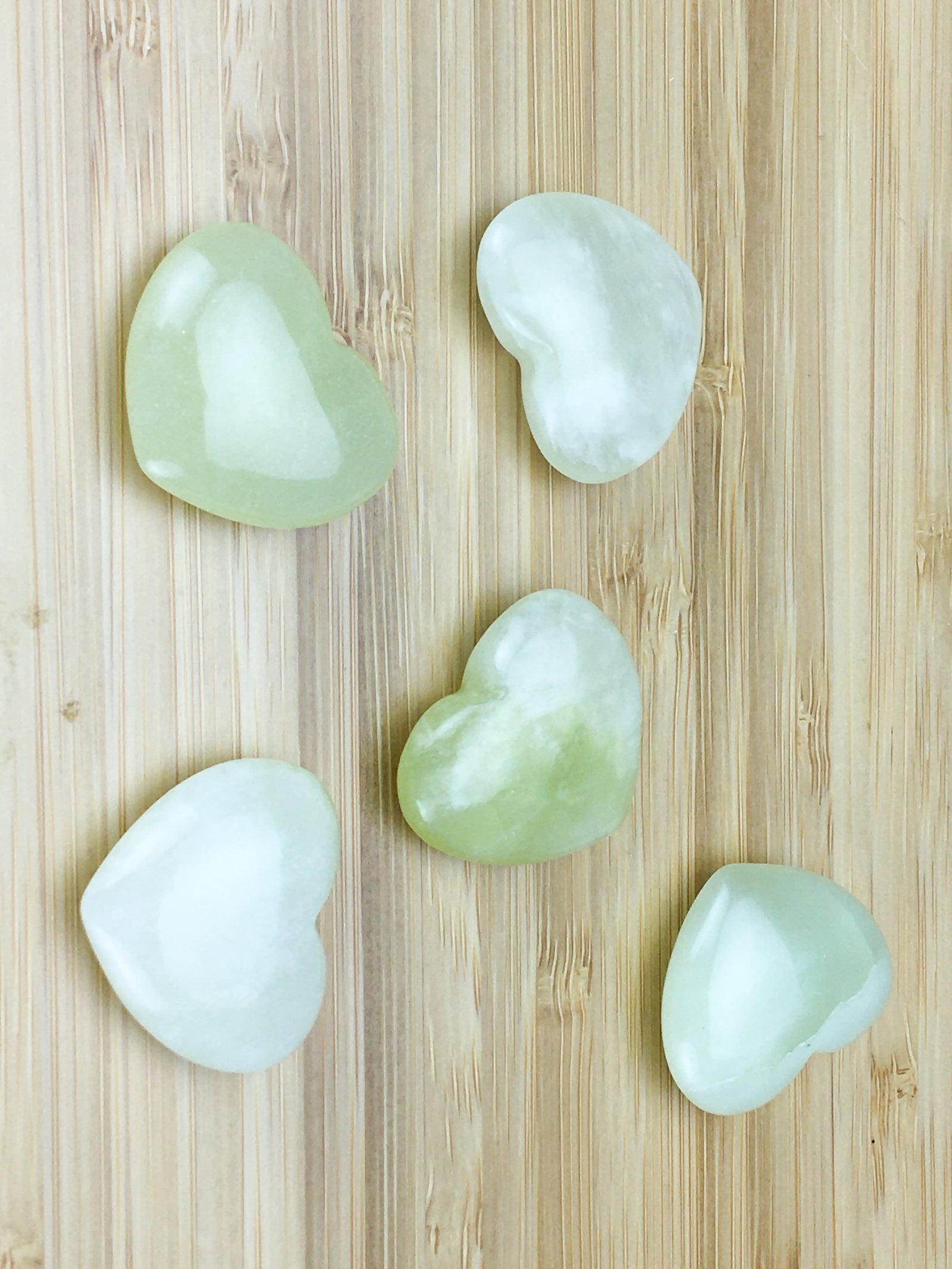 Five bowenite hearts on a light wood grained surface