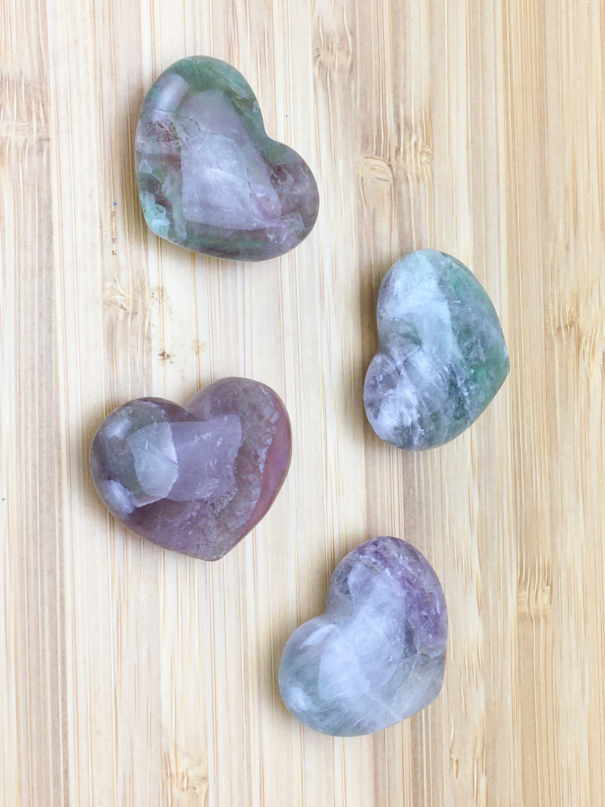 four rainbow fluorite hearts on a light wood grained surface.