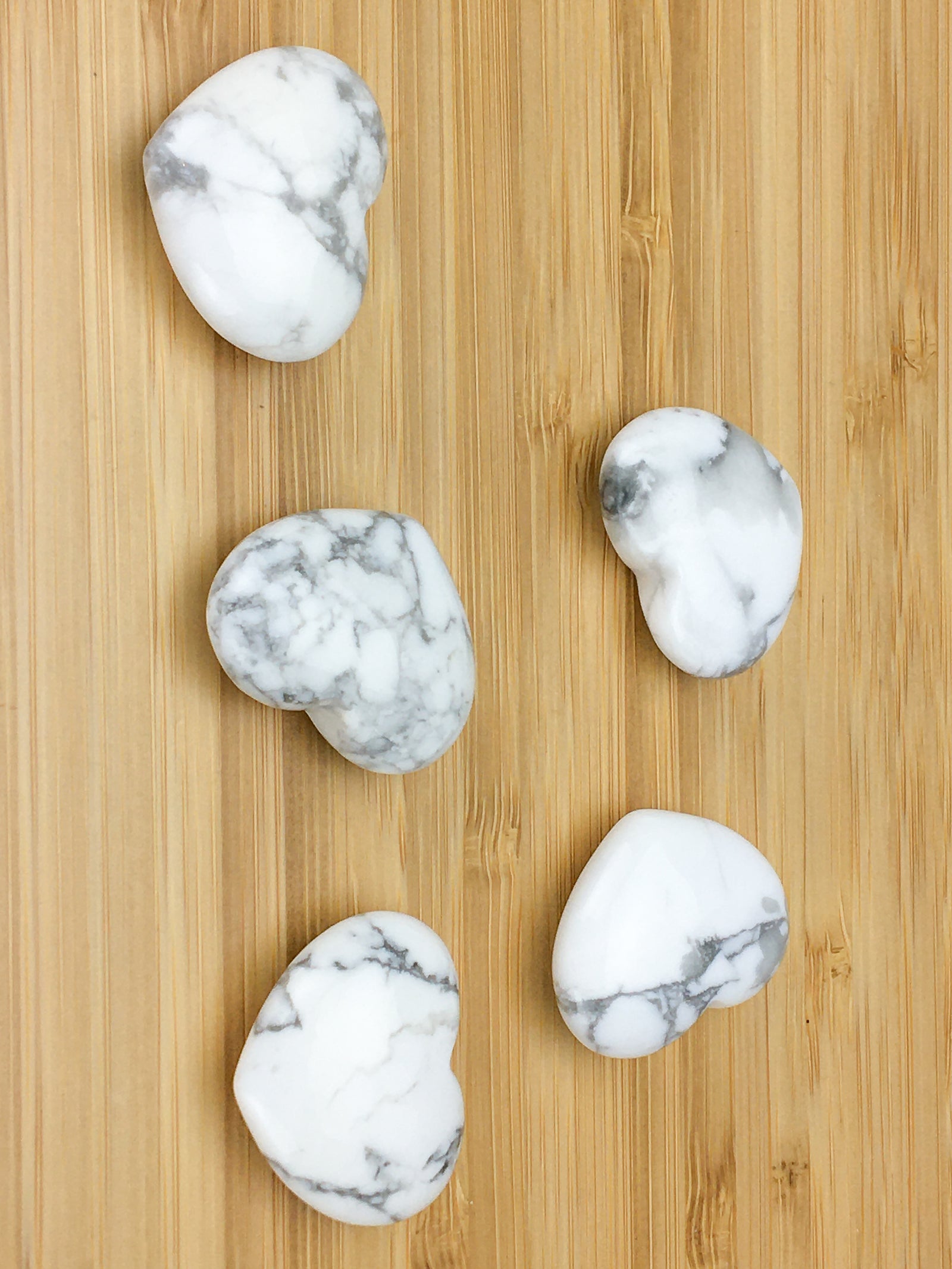 five howlite hearts on a light wood grained surface