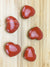 five snakeskin jasper hearts on a pale wood grained surface.