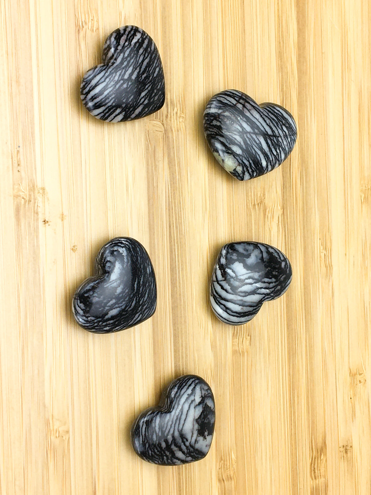 Five net jasper hearts on a light wood grain surface