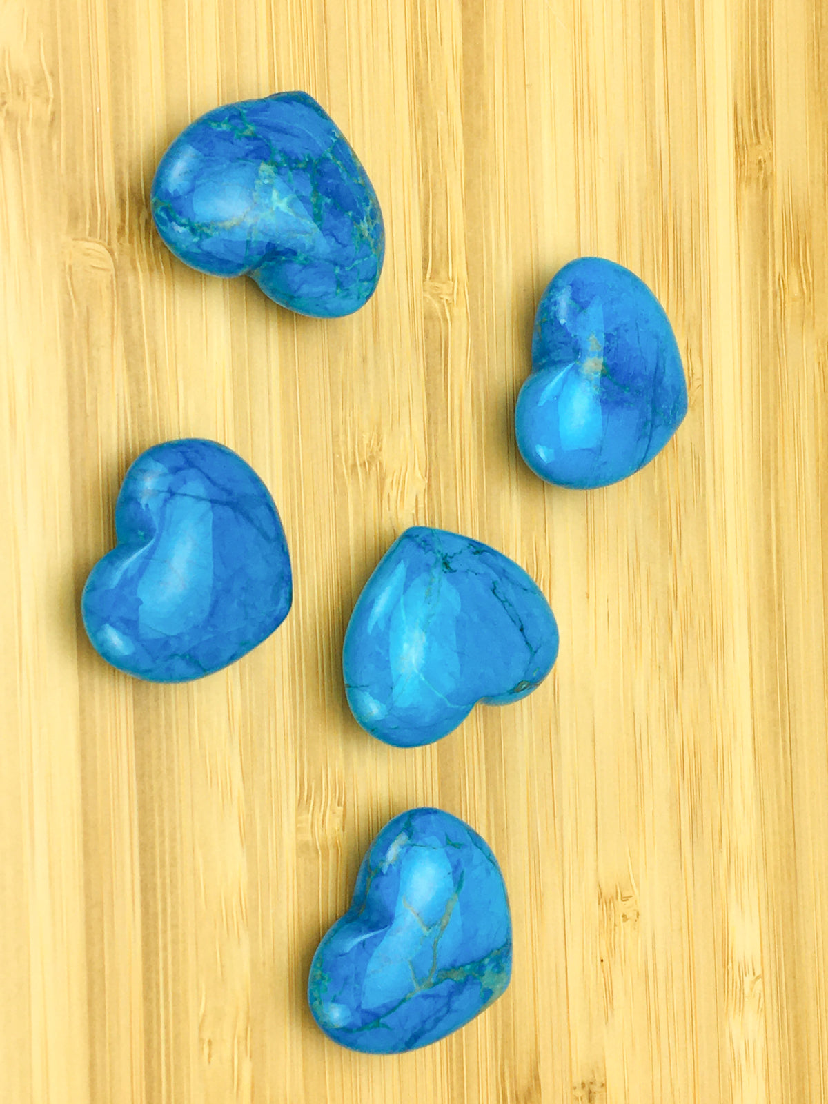 five blue howlite hearts on a light wood grained surface.