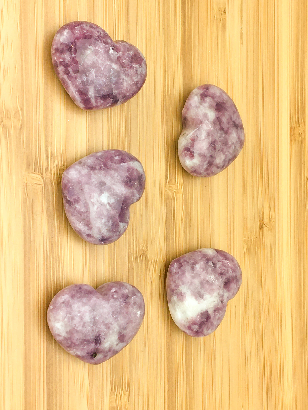 Five lepidolite hearts on a light wood grained surface