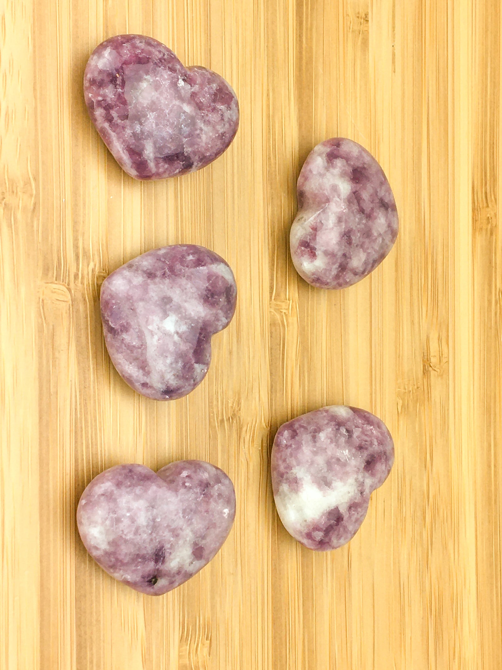Five lepidolite hearts on a light wood grained surface