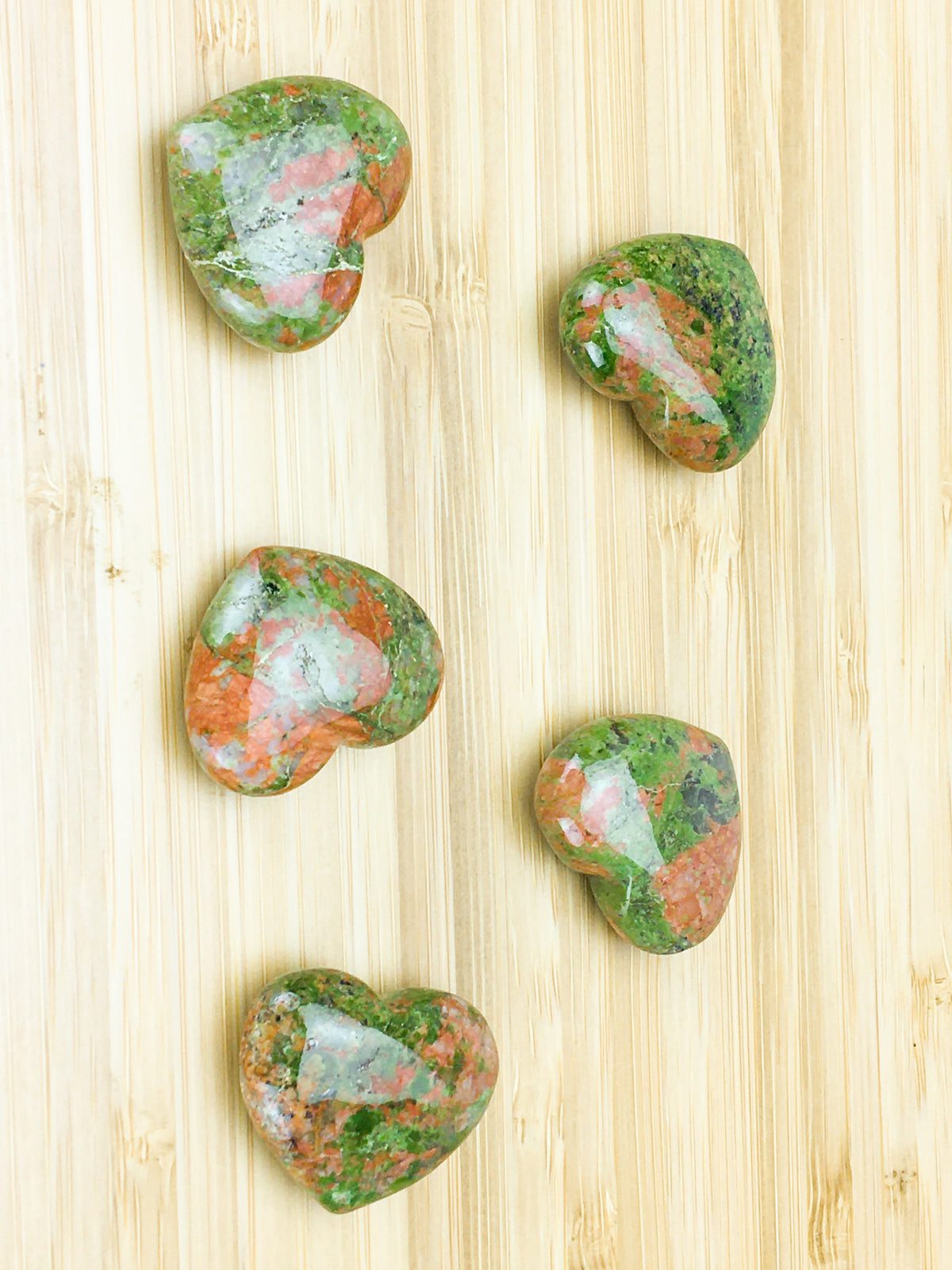 Five unakite hearts on grsinedcwood. The unakite consists of green epidote with crystals of orthoclase 