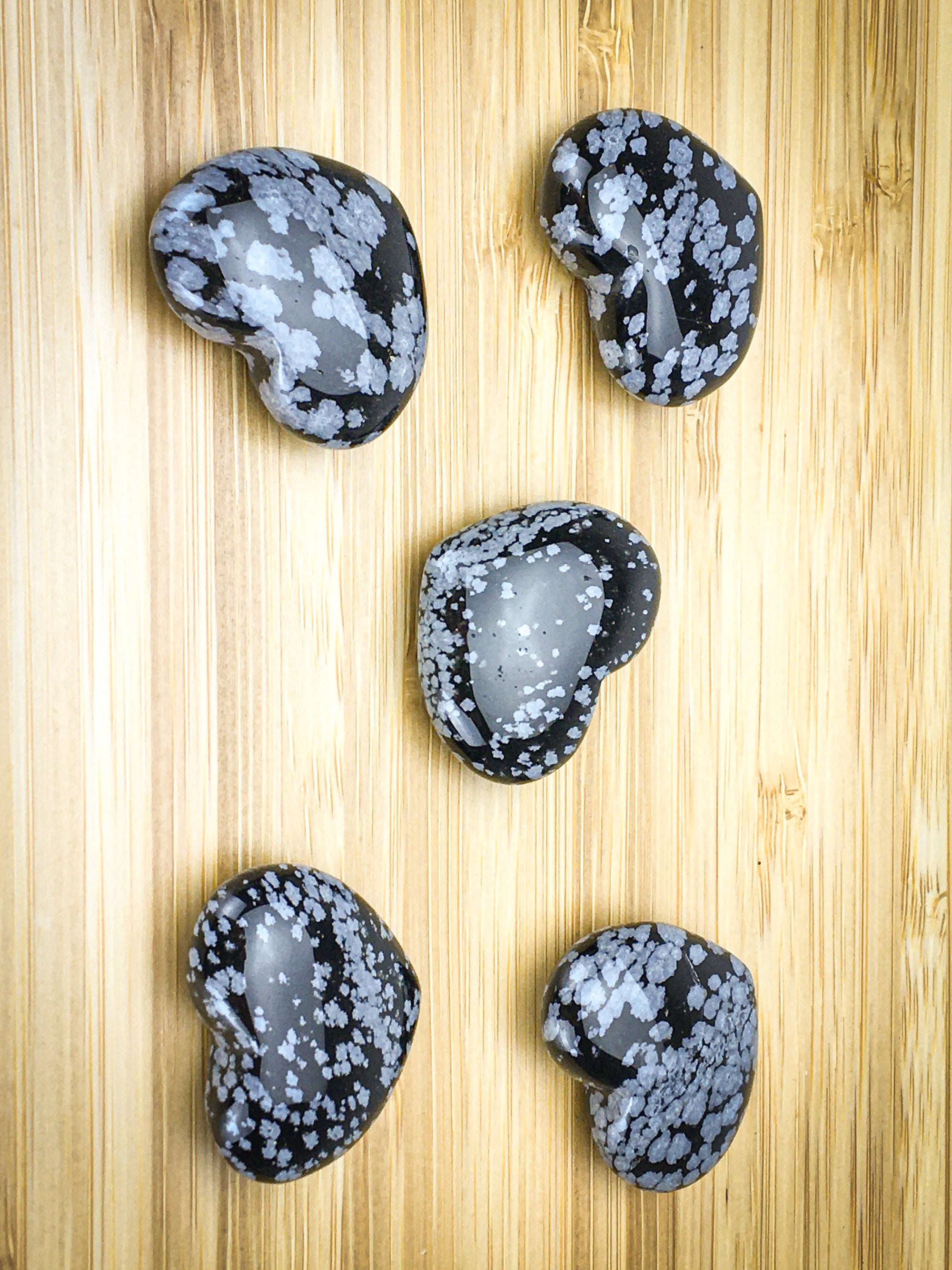Five snowflake obsidian hearts on a light wood grain surface