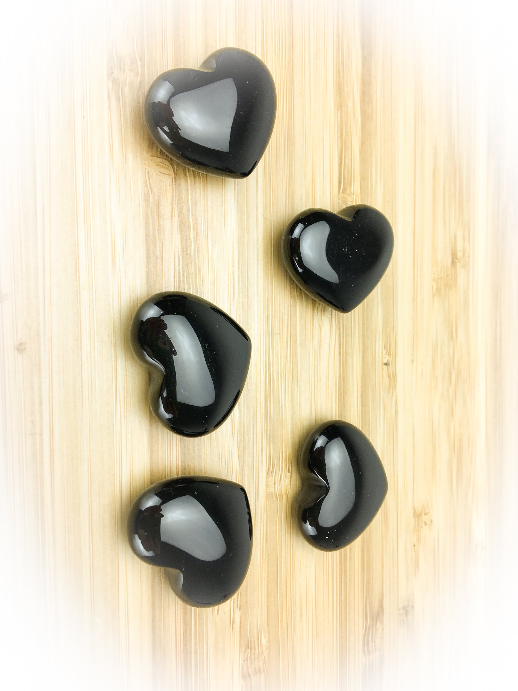 five obsidian hearts on a pale wood grain surface