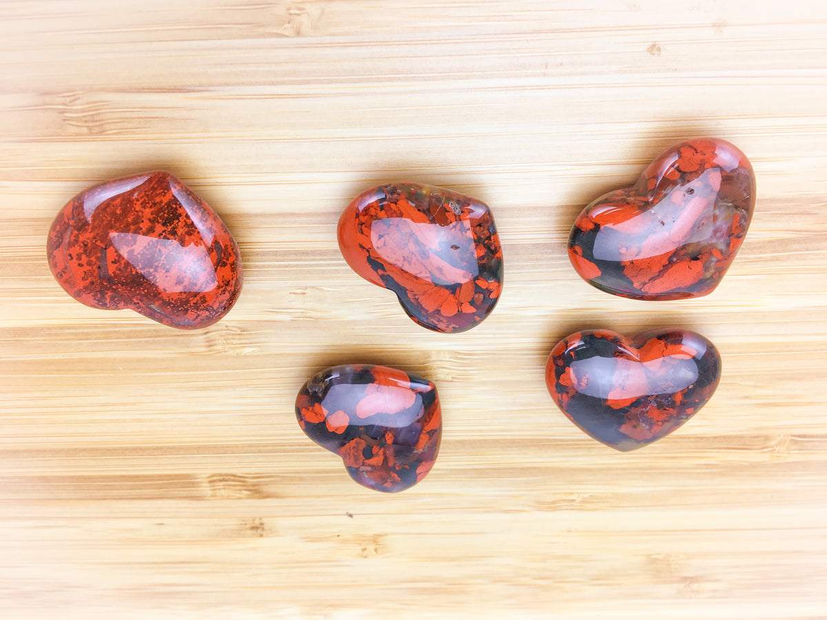 five red poppy jasper hearts on a light wood grain surface