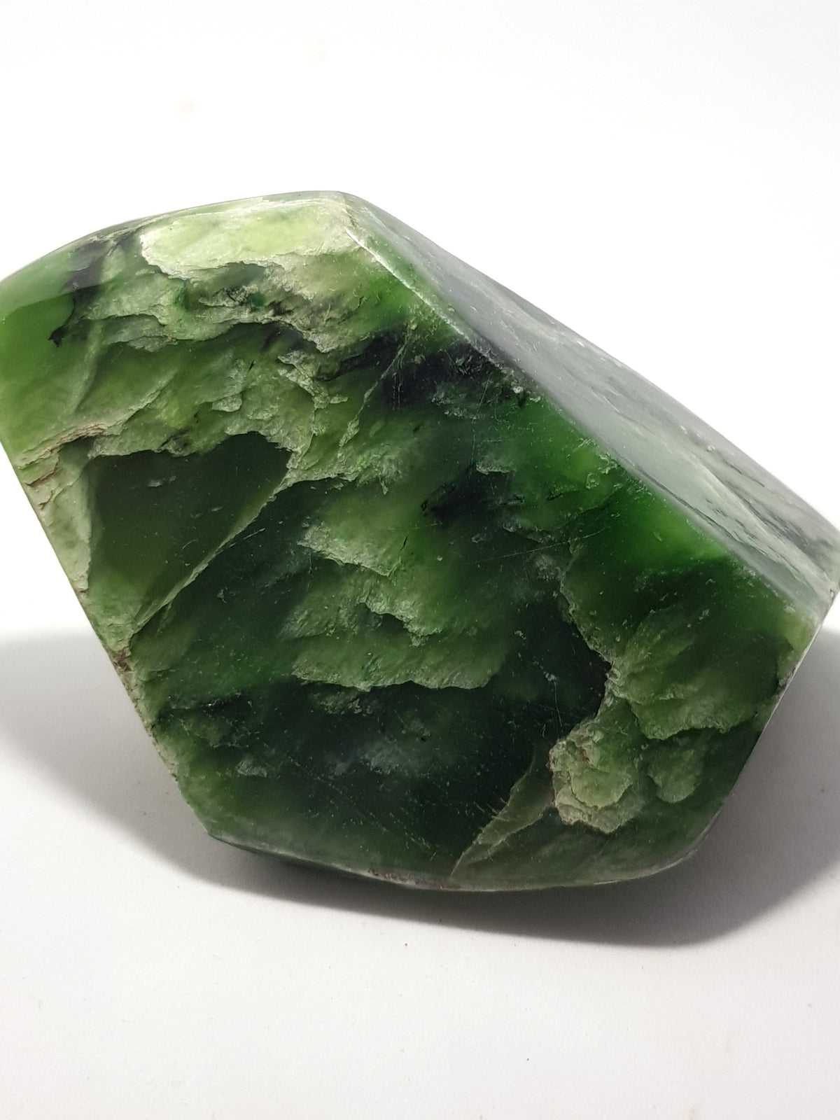 an angular freeform of nephrite jade. It is a rich green with creamy green patterns which look like trees or waves.