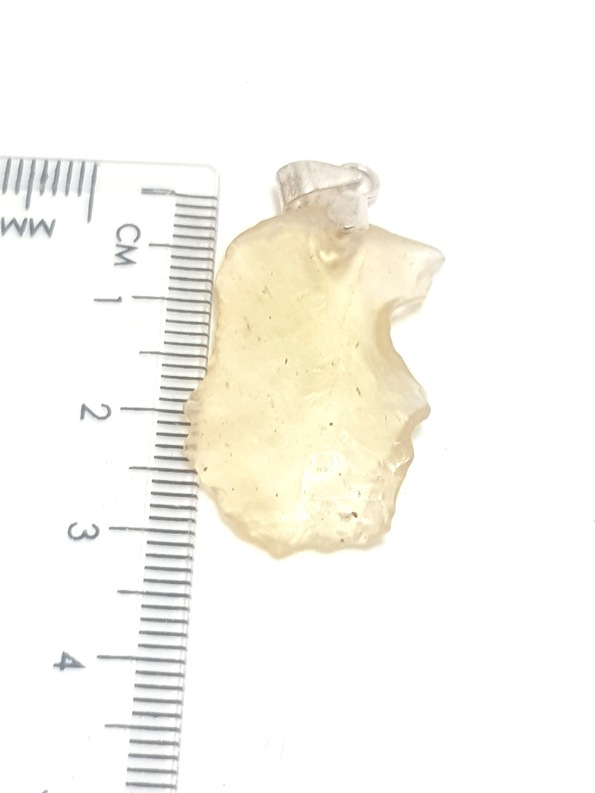 a piece of libyan desert glass against a see through plastic ruler. The sample is 3cm. The libyan desert glass is yellow and translucent with an irregular surface