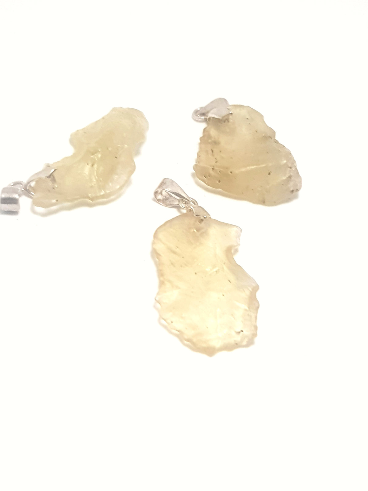 three pieces of libyan desert glass. They have a metal pennant attached on  one end, they are pendants