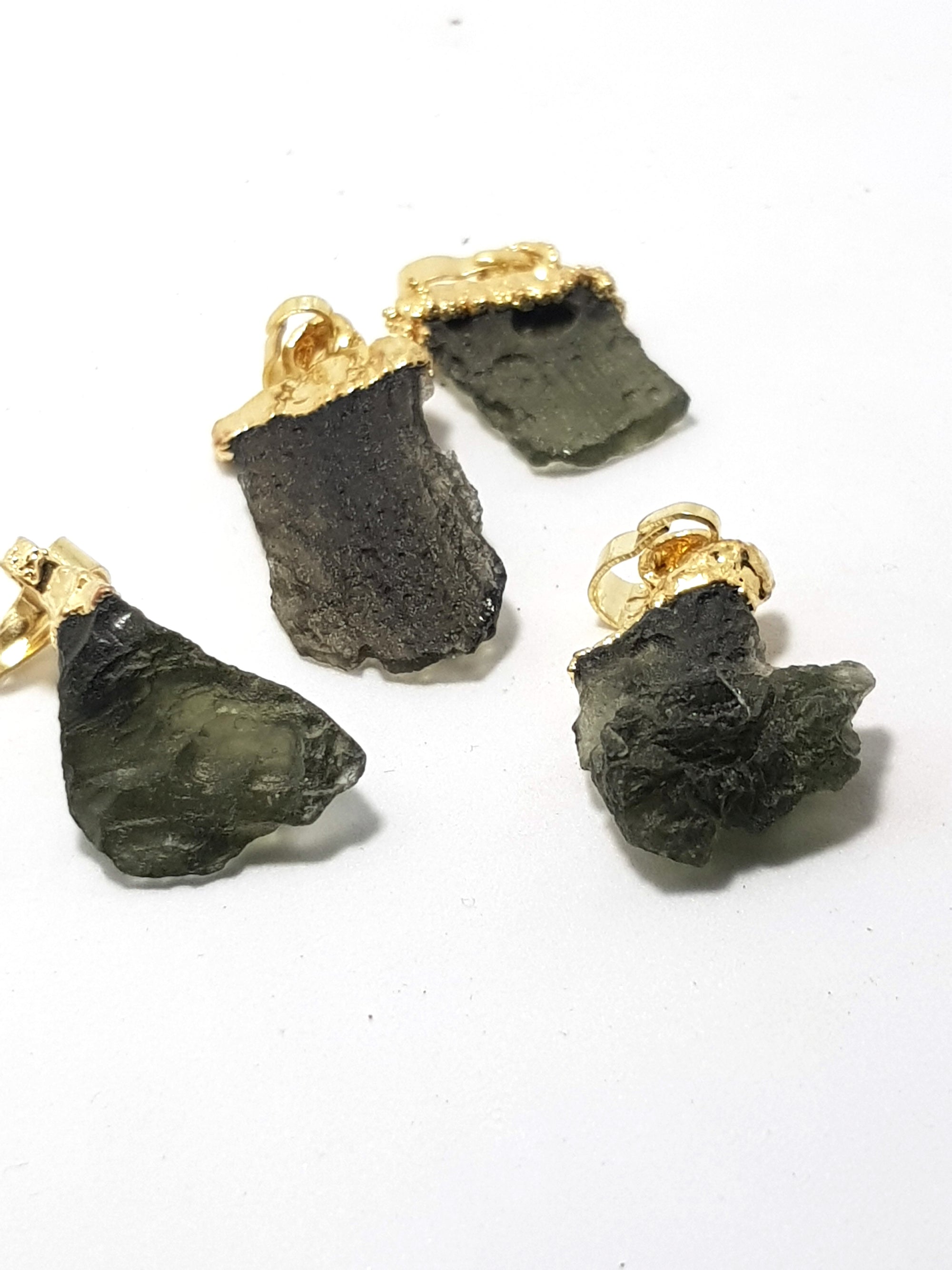 four moldavite pendants. The samples are green, translucent and have the distinctive wrinkled rind. They are end capped with a gold coloured material to make pendants.