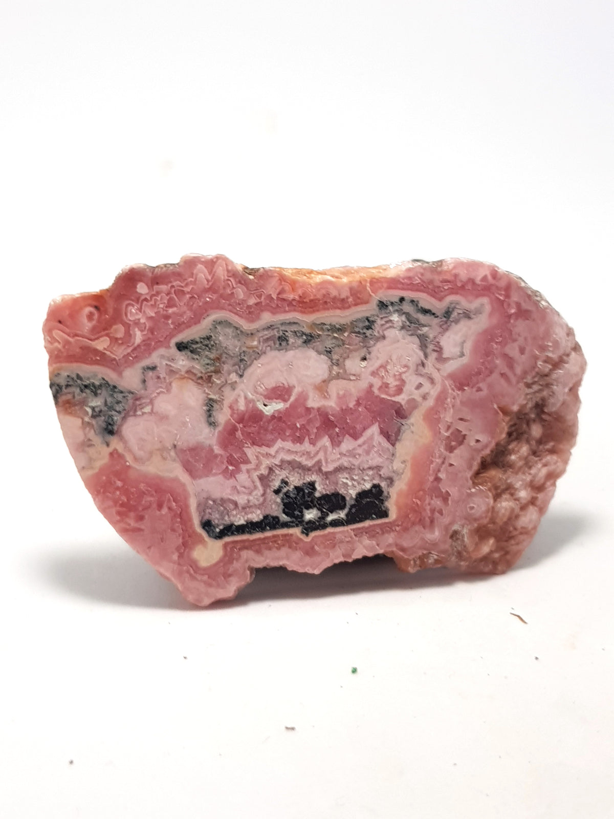 Rhodocrocite slice. It is banded. The bands are different shades of pink. There is are black and grey bands n the centre of the sample.