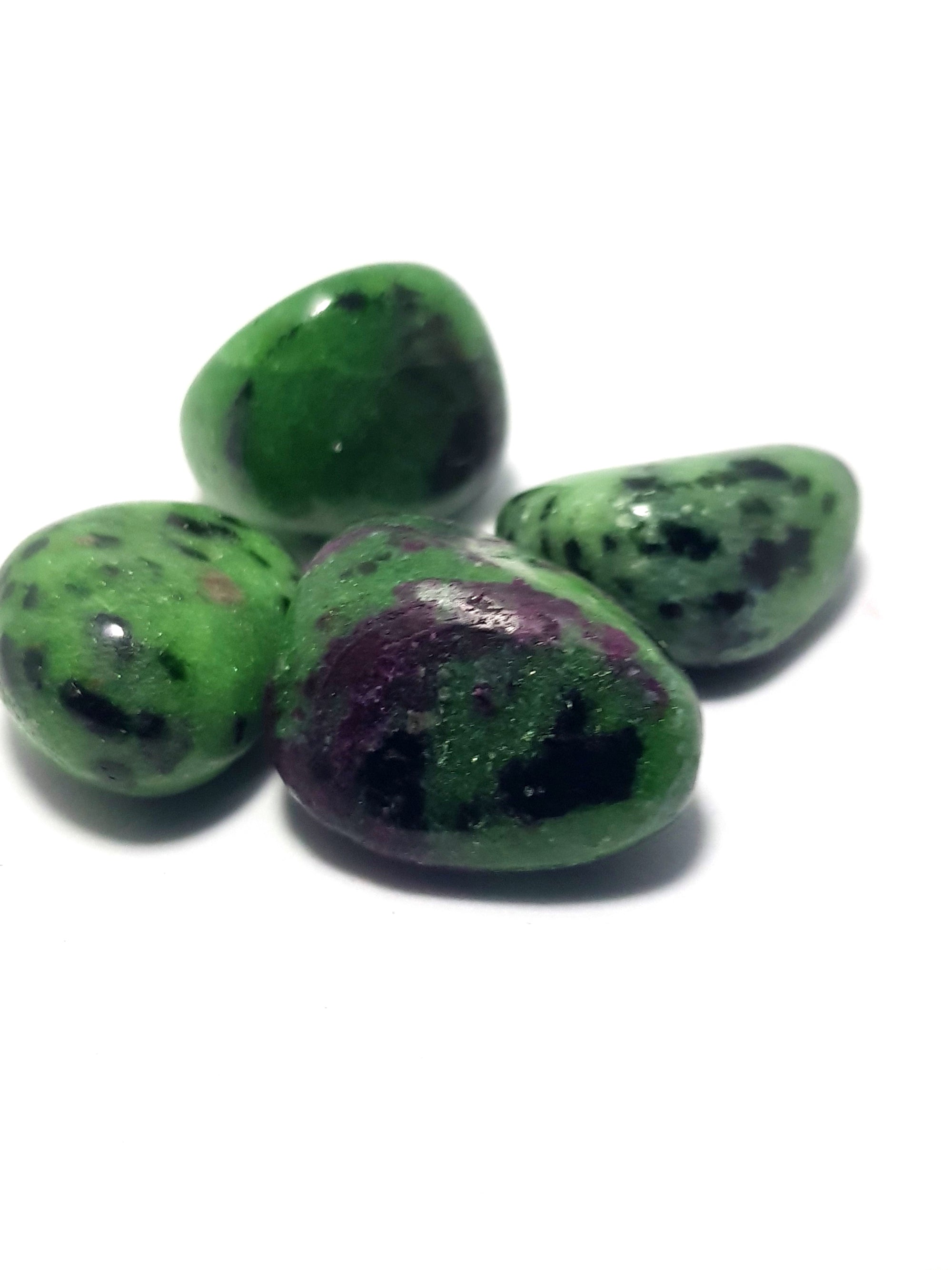 four tumbled pieces of red corundum (ruby) in Zoisite. The corundum is visible as a large purple red patch in the central sample of the image. The zoisite is pistachio green and sparkly. It contains black dots throughout.