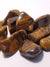 tumbled pieces of tiger eye. The pieces are banded - the bands are dark brown and golden. The samples show chattouyancy