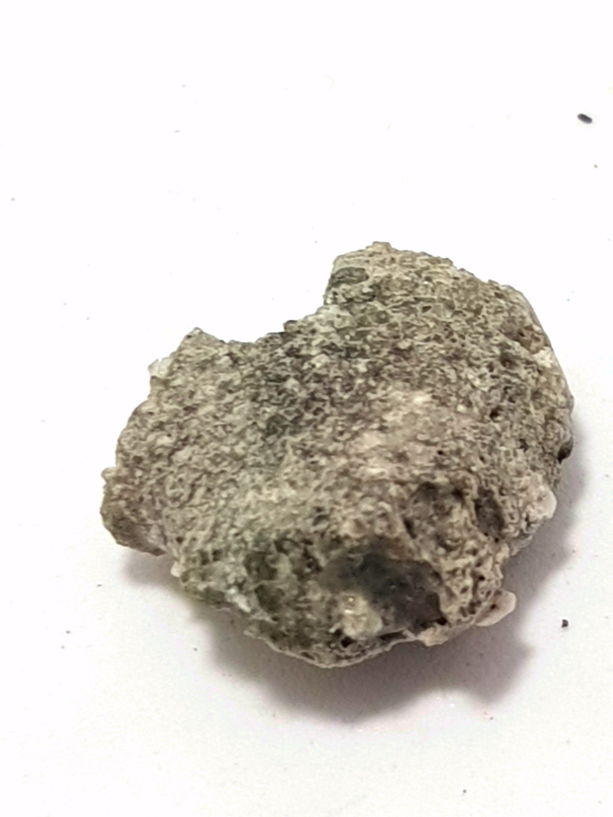 sample of trinitite. It is a single piece. It is dark green/brown. The surface is smooth, but the sample is rough at the edges. It does not appear to have been broken and looks like one single piece.