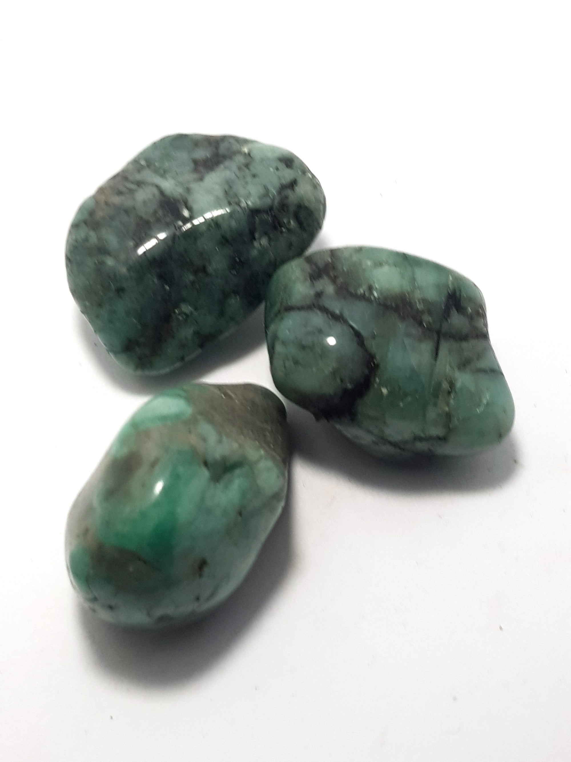 Tumbled emeralds. They are a deep green with black veining. The pieces are polished but  irregularly shaped.